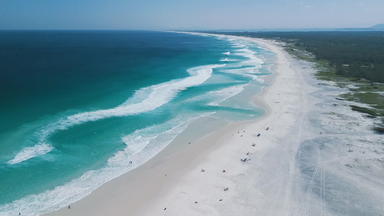 Aerial flies over Praia Grande beach, white sand, blue ocean, and waves to horizon at Arraial do Cabo
