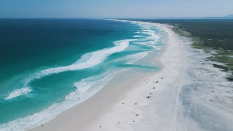 aerial flies over praia grande beach, white sand, blue ocean, and waves to horizon at arraial do cabo