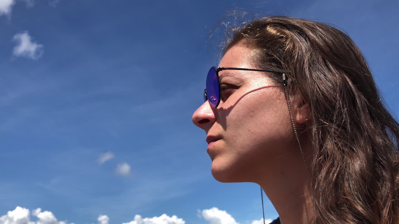 White girl wearing sun glasses looks around with blue sky on background, slowmotion