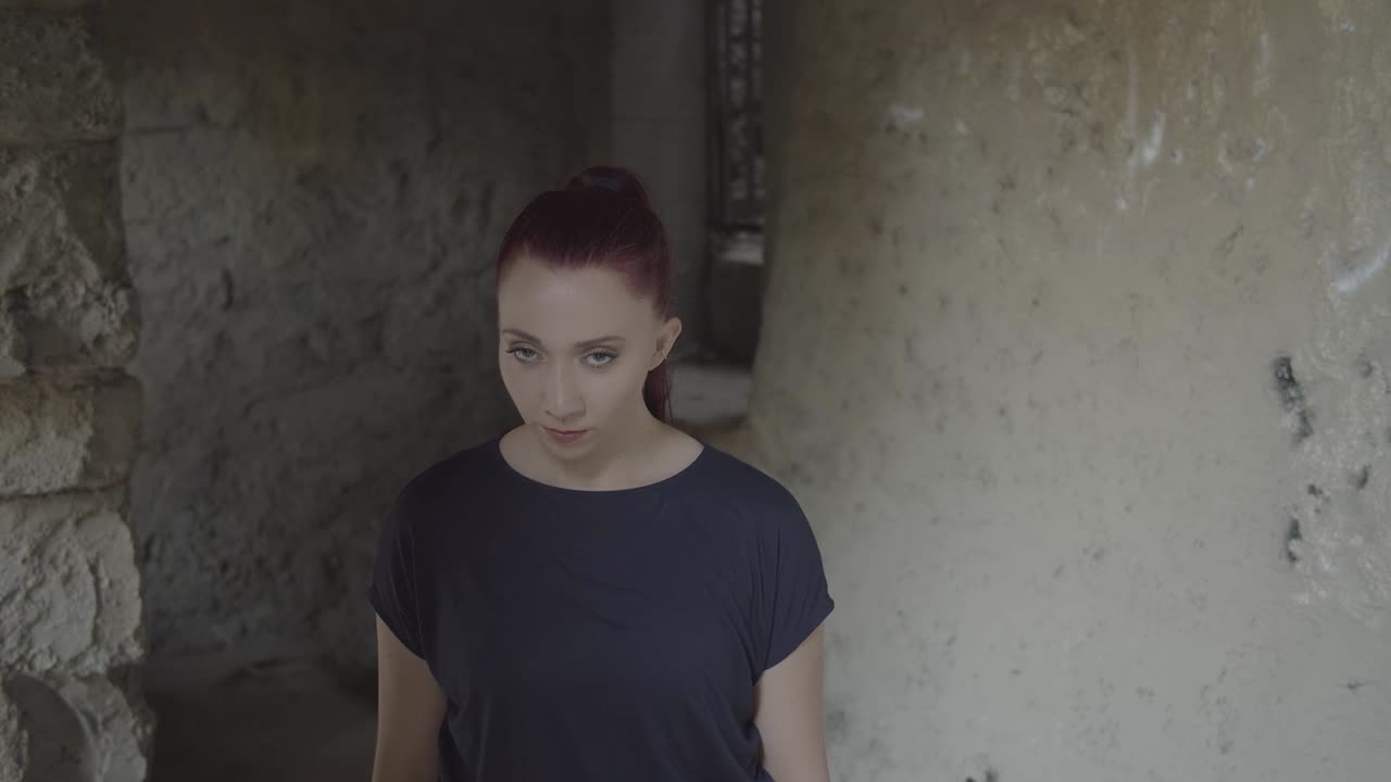 retrato de una mujer joven en un antiguo monumento de piedra se para y mira extrañamente antes de levantar la cabeza y cerrar los ojos