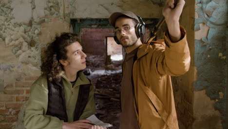 two production coworkers talking while reading a document and holding a microphone during recording of a movie in a ruined building