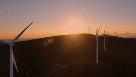 orange and red glow of a sunset behind the mountain s giant windmill turbines produce clean energy