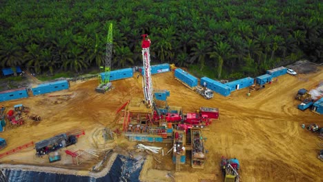 Cinematic-Drone-Footage-of-Onshore-Drilling-Rig-equipment-structure-for-oil-exploration-and-exploitation-in-the-middle-of-jungle-surrounded-by-palm-oil-trees-during-sunset-and-high-oil-price