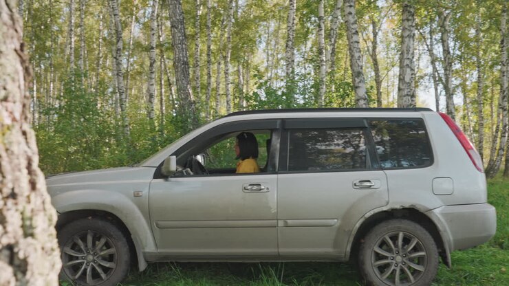 Un homme gare sa voiture dans les bois. Un visiteur arrive en véhicule sur un site boisé. Un individu sort d'un SUV dans une clairière au milieu des arbres. Un voyageur gare un véhicule blanc en forêt et commence à installer le campement.