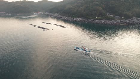 aerial panoramic drone fly above japanese sea with fishing boat sailing boathouses houses hills and sunshine through kyotango kyoto japan, beach travel destination in asia