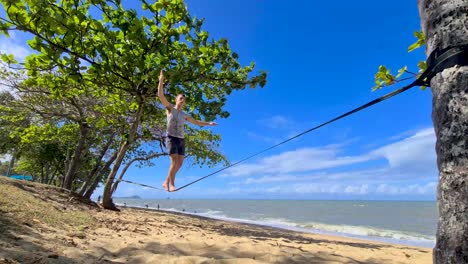 macho adulto joven caminando lentamente a lo largo de slackline en trinity beach en cairns