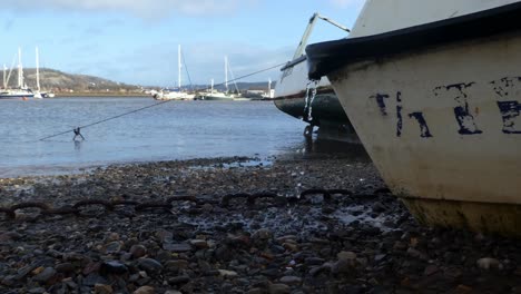 leaking boat moored on pebble beach with rusty chain at low tide