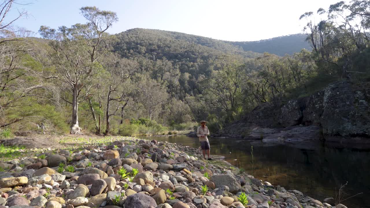 bosquiman australiano pescando en un río con montañas épicas en el fondo