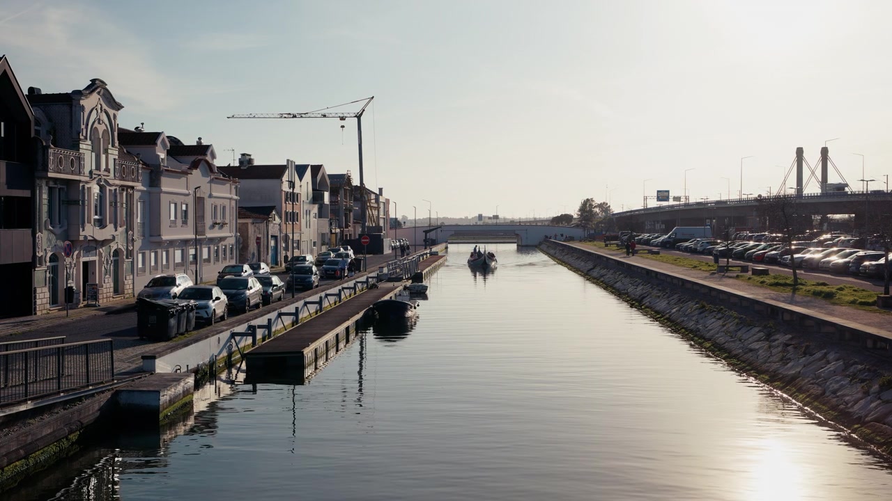 Una tradizionale barca moliceiro scivola lungo un canale calmo ad Aveiro, Portogallo, affiancata da eleganti facciate Art Nouveau e riflettendosi nell'acqua immobile in una luminosa mattina d'inverno