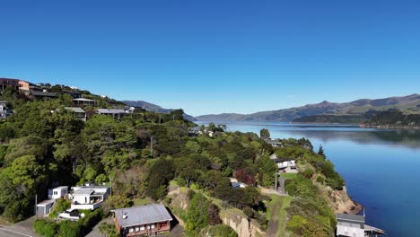 drone footage captures akaroa's serene bay, lush greenery, and coastal houses under clear skies