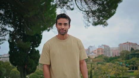 latin guy posing green park in front cityscape close up. man looking camera