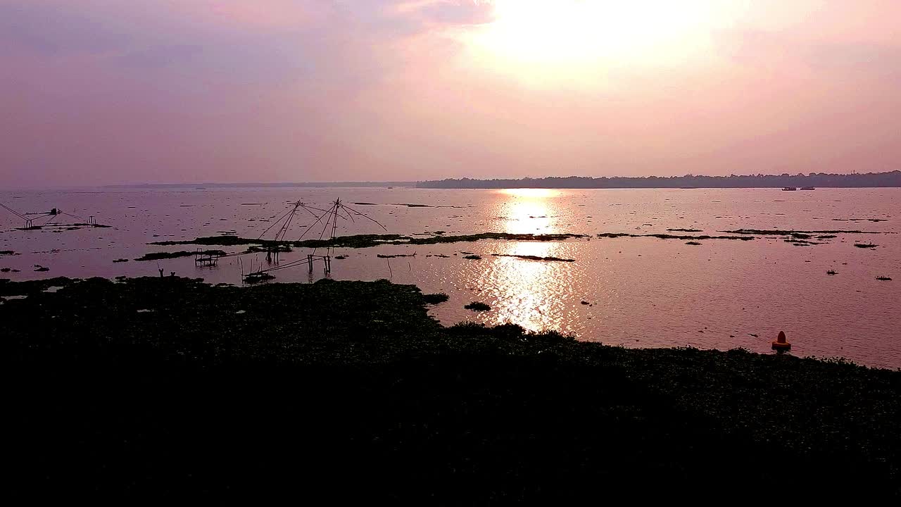 Solnedgang over Keralas elvemunninger med silhuetter av kinesiske fiskegarn og palmer