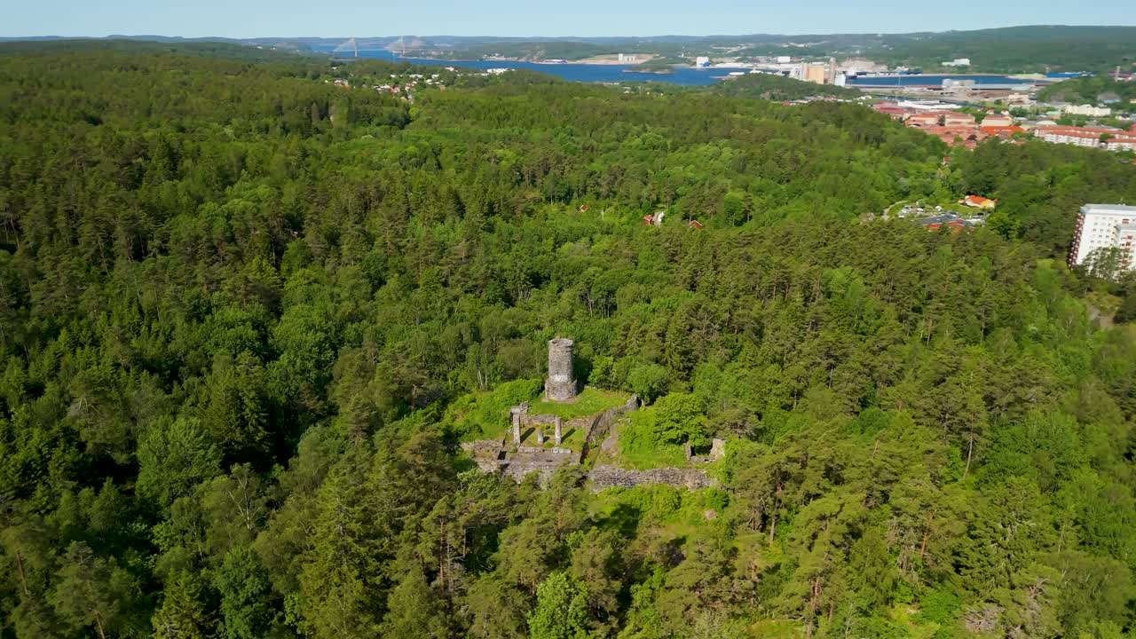 Parallasse aerea delle rovine del castello medievale di Tureborg Slott con torre di pietra rotonda che si erge da una fitta foresta di pini sopra Uddevalla, Svezia