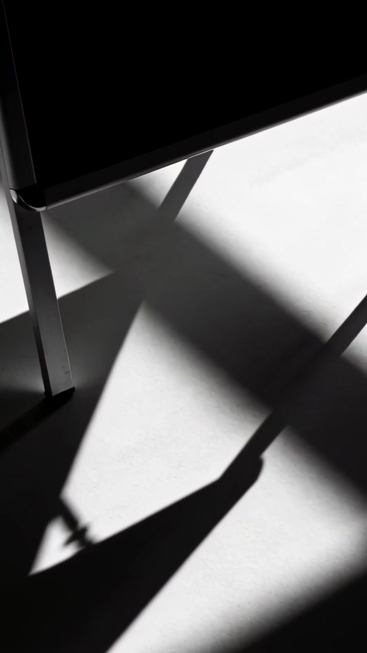 Vertical video: Moving light casting angled shadow on studio floor by metal leg and black seat edge