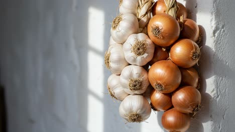 a beautiful arrangement of fresh garlic and onions hanging outside against a sunlit background, showcasing their natural colors and textures in a charming culinary display