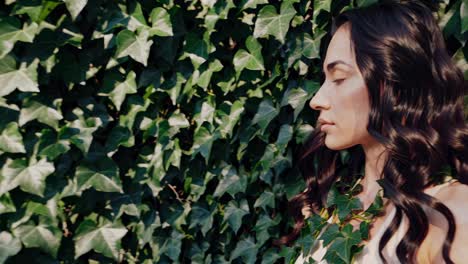 woman with long, flowing hair stands peacefully against a vibrant wall of ivy. her eyes are closed, suggesting a moment of tranquility and connection with nature