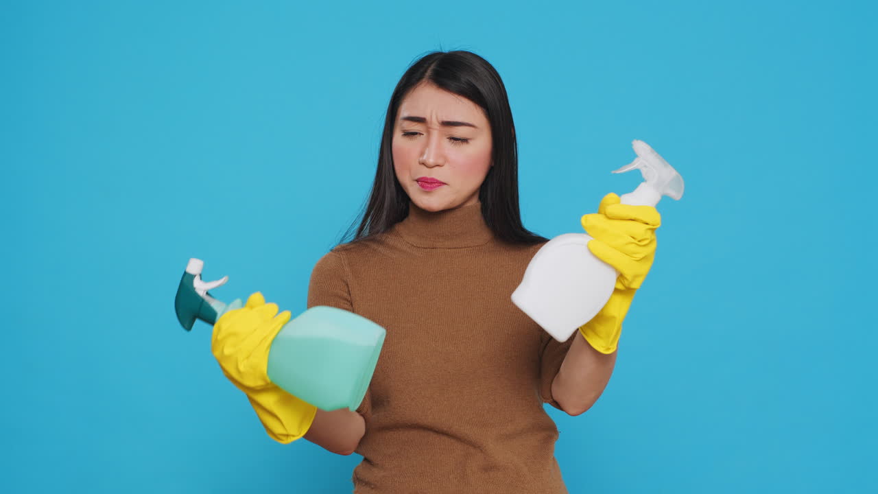Cheerful house cleaner wearing yellow rubber gloves while showing chemical detergent spray