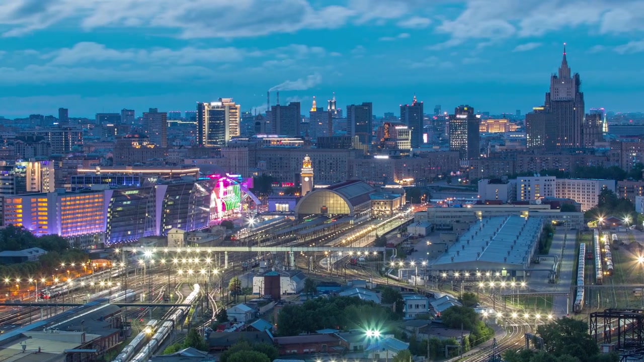 Kiev Tren İstasyonu'nun gece-gündüz geçişli hızlandırılmış panoramik kuşbakışı görüntüsü ve Rusya, Moskova'daki modern şehir. Trenler ve demiryolu hatlarıyla havadan çatı manzarası. Yukarıdan aydınlatılmış binalar.
