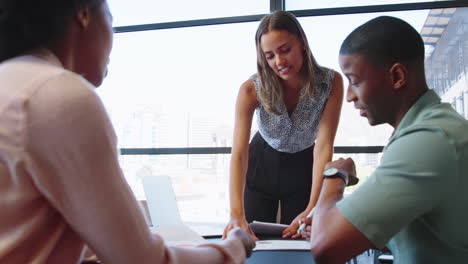 Multi-Cultural-Business-Team-Meeting-Around-Office-Boardroom-Table-With-Laptops-Discussing-Documents