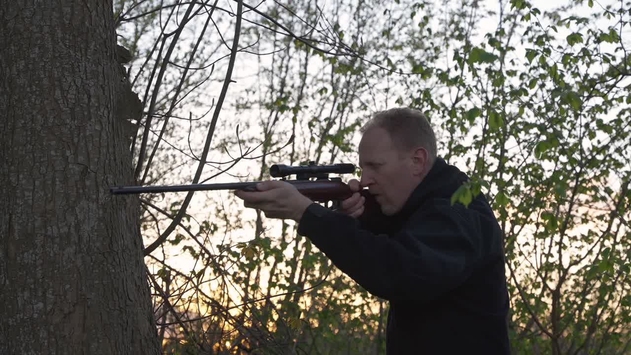 Hunter aiming rifle at sunset in the woods