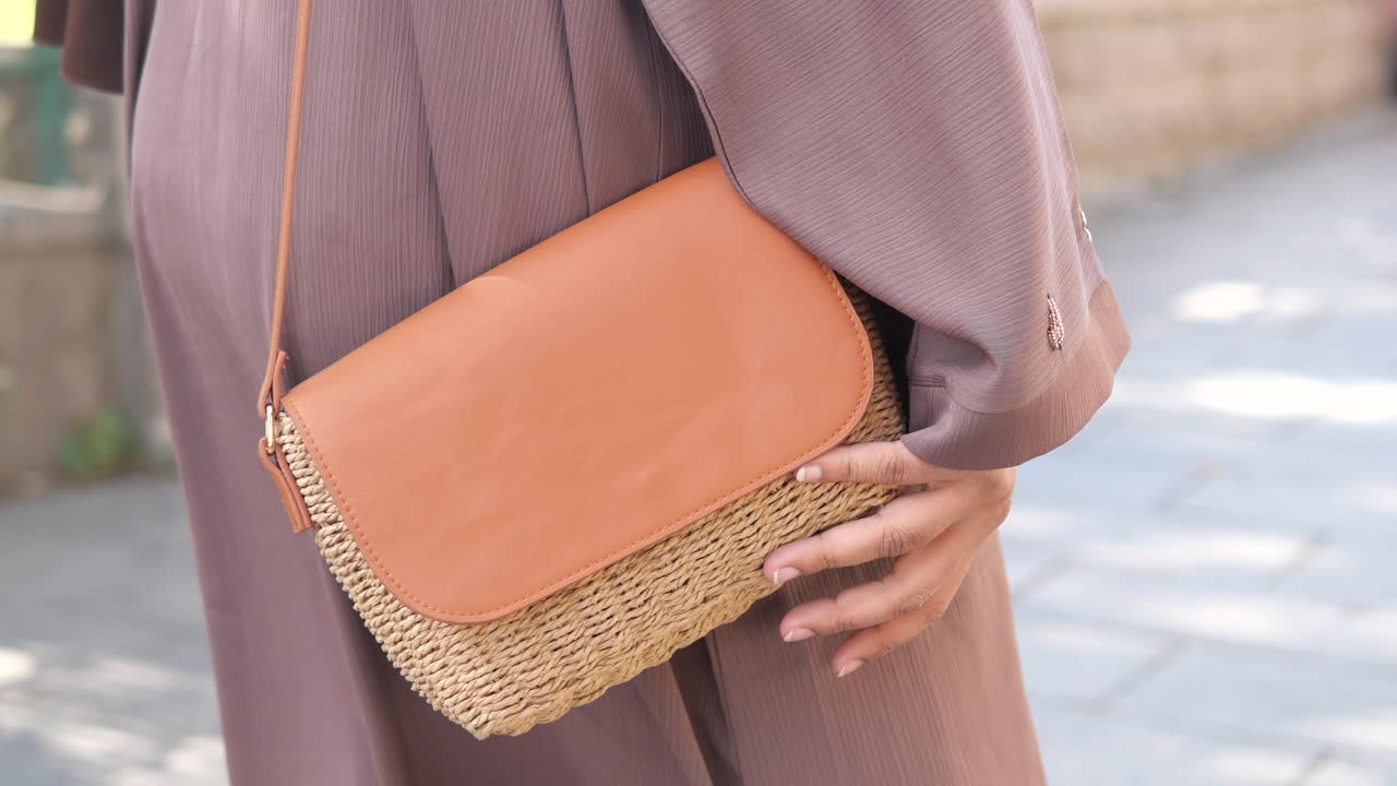 Woman carrying a straw handbag on a city street.