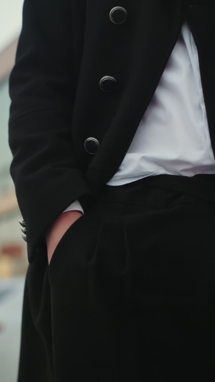 inversor en abrigo negro comprobando el tiempo con mirada confiada y mano derecha en el bolsillo, de pie frente a un moderno edificio de vidrio, empresario exitoso que irradia confianza en el entorno urbano