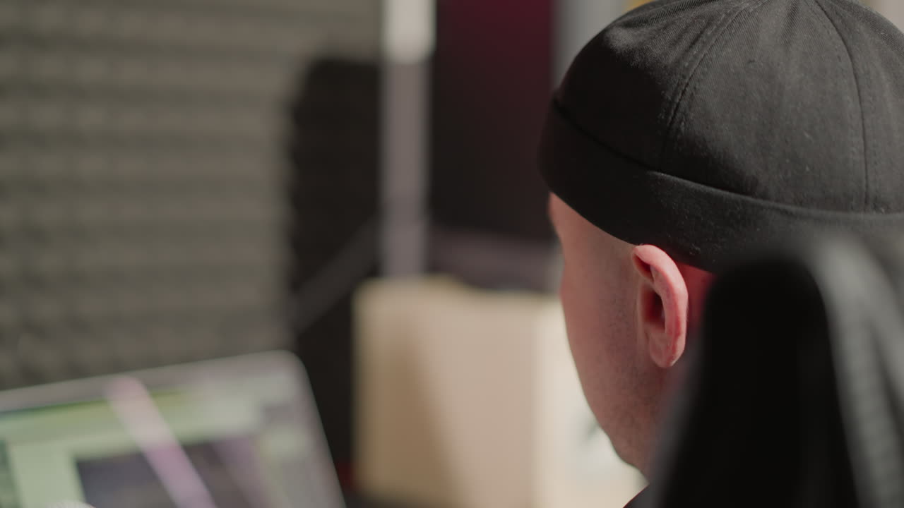 검은 모자를 입은 남자의 얼굴의 클로즈업, 그의 앞에 있는 무언가를 쳐다보면서 미소. 흐릿한 배경에는 컴퓨터 스크린이 보인다