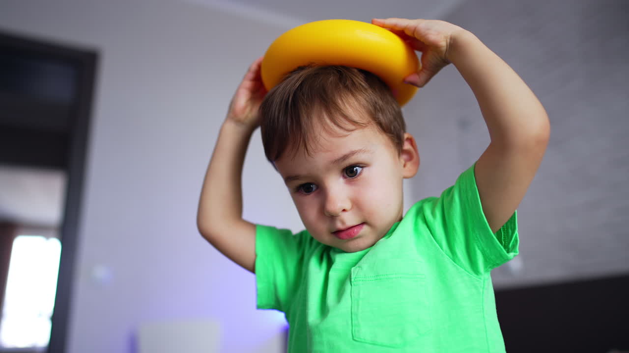 Happy Caucasian kid holding a yellow ring from toy pyramid on his head. Smiling toddler's portrait from low angle view.