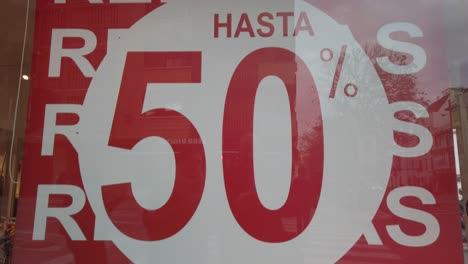 Half-off-clearance-sign-in-store-window-in-Spanish-writing,-Tilt-Down