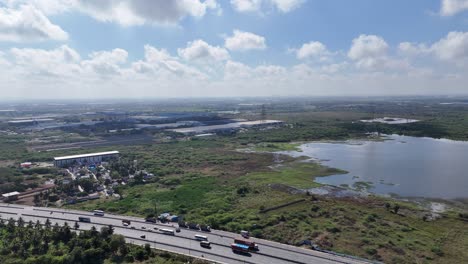 aerial view of a busy chennai highway runs alongside a large, natural lake and wetlands. trucks indicate active logistics near developing land. perfect for infrastructure and environmental themes