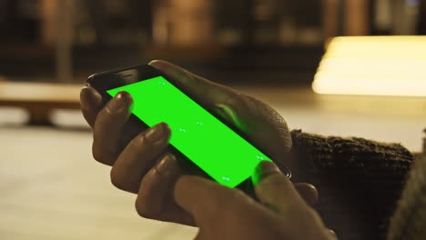 close up view of unrecognizable hand holding vertically modern luxurious chromakey screen smartphone on bright blurred city lights background