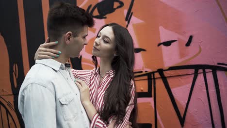 una pareja abrazándose frente a una pared de graffiti.