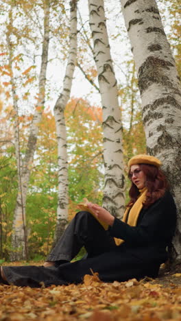 dama elegante en la soledad se apoya contra el árbol volviendo a través del libro pensativo, rodeada de hojas doradas de otoño, ella abre cuidadosamente la página, perdida en profunda contemplación