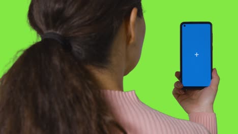 vista trasera de la mujer transmitiendo contenido a la pantalla azul del teléfono móvil contra la pantalla verde