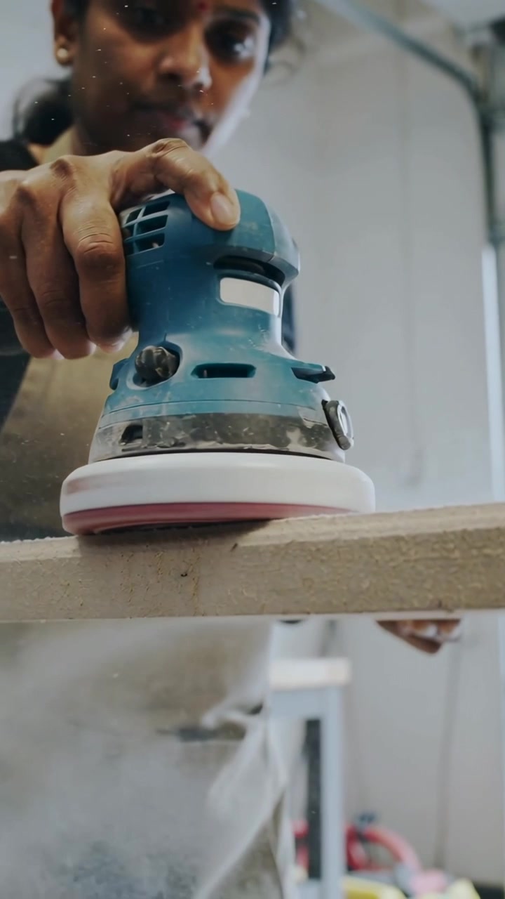Vertical video: Placing blue sander, Indian carpenter in apron sanding plank on bench for finish