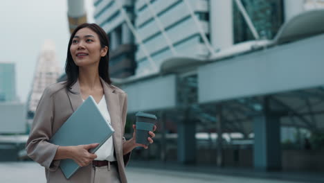 businesswoman walking in city with laptop and coffee