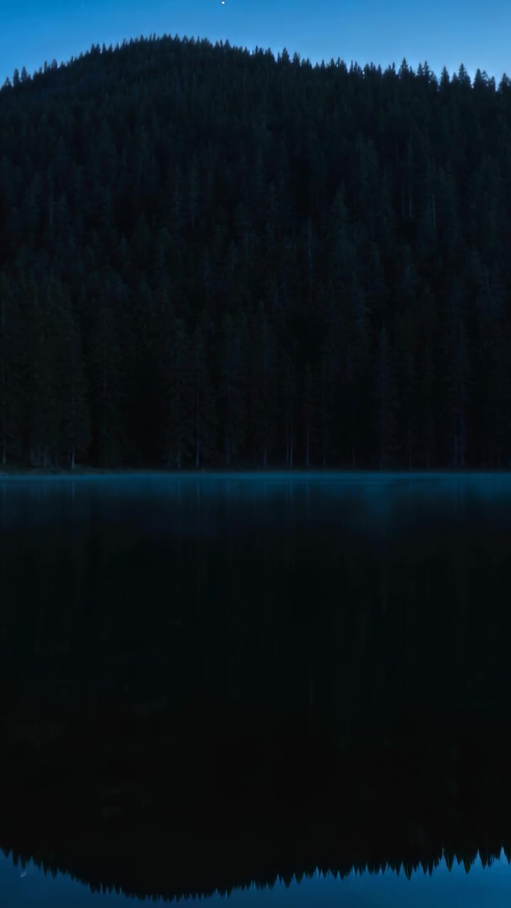 Vertical video: Showing fir ridge at lake and mirror shifting as dusk falling and mist forming