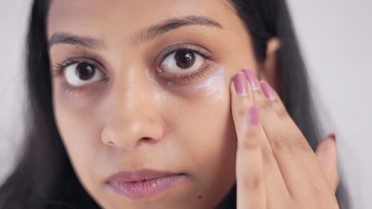 Close up shot of a young woman applying moisturizing cream on her under eye area, skin care concept.