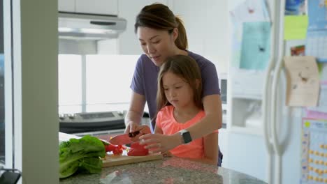 Mother-teaching-daughter-to-chop-vegetables-in-kitchen-4k