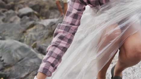 mujer afroamericana recolectando basura en las rocas cerca del mar