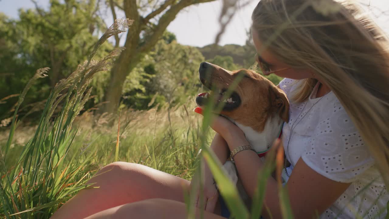 Young woman sitting in long grass with pet dog bonding