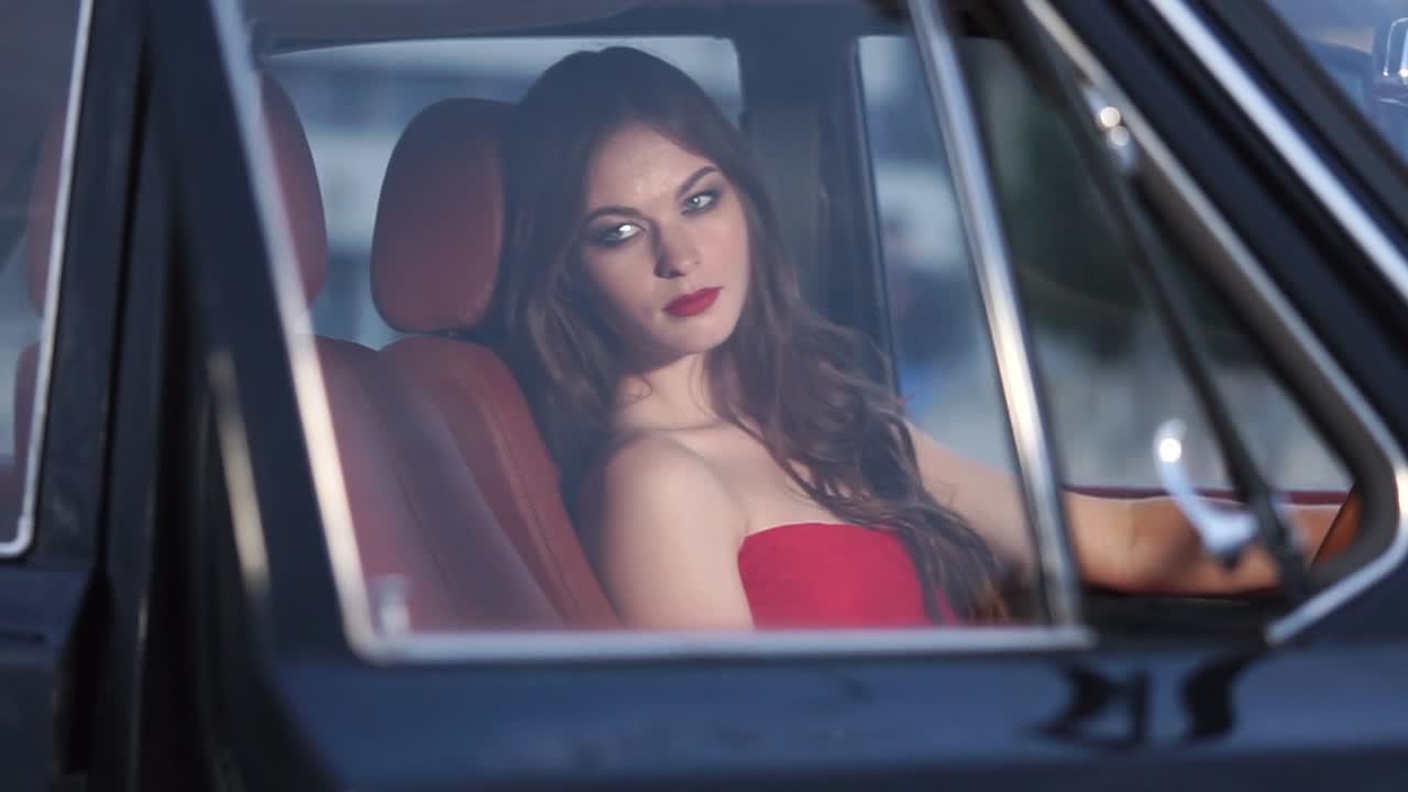 Mulher de vestido vermelho dirigindo um carro vintage