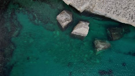 top down view of il-kalanka beach in malta with turquoise water, splashing on the limestone wall