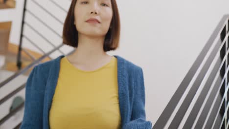 video portrait of happy asian woman smiling to camera, standing on stairs at home