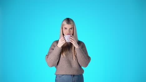 카페 컵에서 커피를 마시며 카메라를 바라보는 예쁜 금발 여성의 초상화, 분홍색 배경으로 촬영된 스튜디오