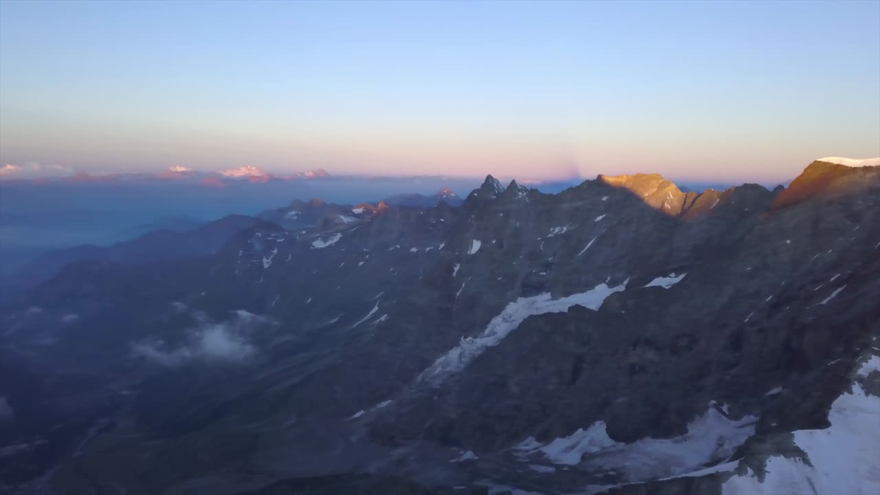 amplia vista aérea desde drones sobre alpes con nieve en empinadas laderas rocosas al amanecer