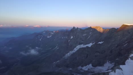 wide aerial view from drone over alps with snow on steep rocky slopes at sunrise
