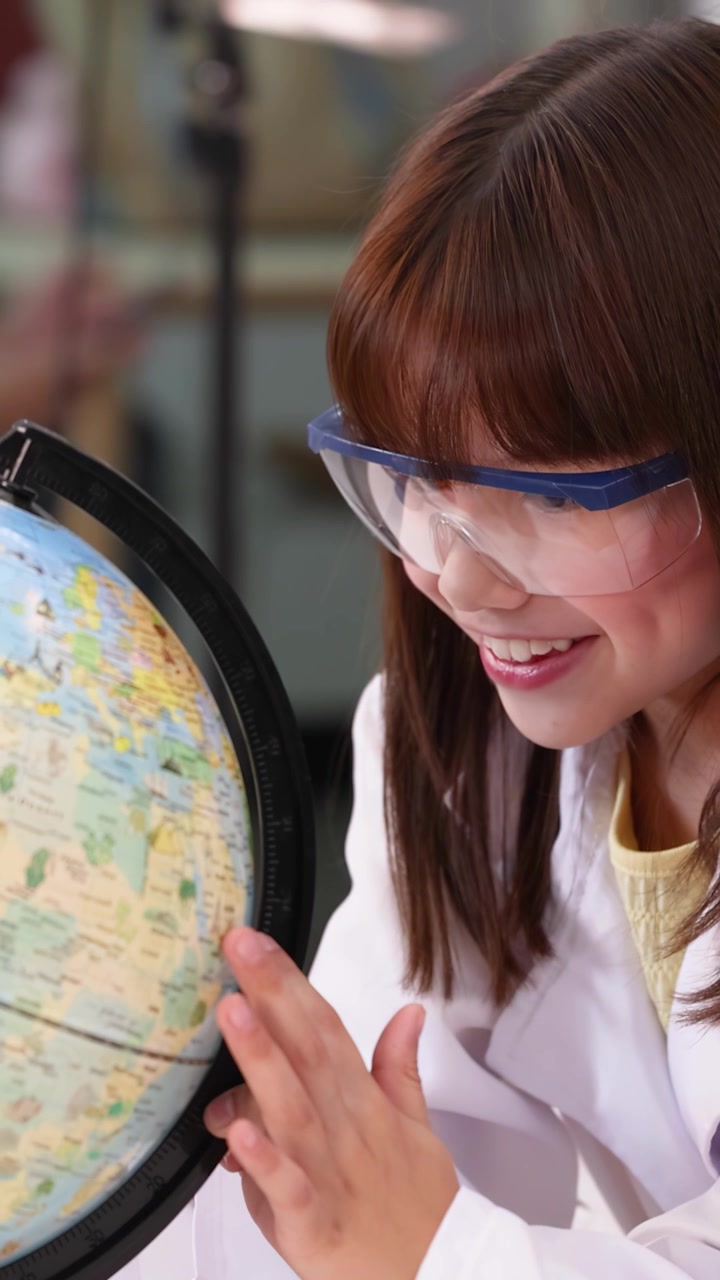 Niña con bata de laboratorio y gafas de seguridad examinando un globo terráqueo