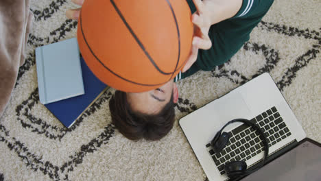 overhead view of asian boy playing with basketball lying on the floor at home