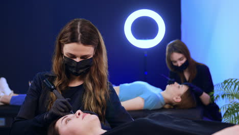 masters of brow make up working in the salon. beauty specialists use tools to perform procedure.